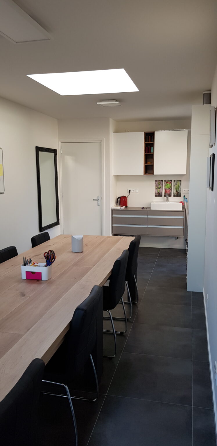 Het atelier in De Maaspoort: werktafels met naaimachines bij het raam.